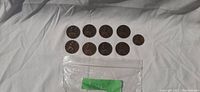 Top view of 10 British coins from 1897 on white cloth background with small plastic bag underneath