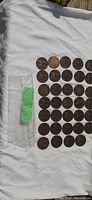 Photo showing a collection of British pennies mainly from 1896 arranged on white cloth with some packaging visible.