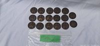 Top view of 21 British large penny coins dated 1899, arranged in three rows on white cloth background, showing the Britannia design