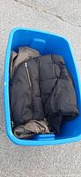 Blue bin containing folded coats including a black puffer coat and tan coat