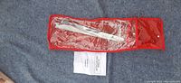 Set of long metal rods in red pouch with clear plastic window and instruction handbook placed outside.