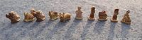 Wide angle photo of all ten Wade Red Rose Tea ceramic figurines in a line on a concrete surface, showing sunlight shadows and details.