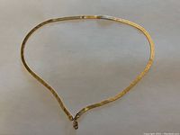 View of entire flat mesh chain necklace laid flat showing Greek key pattern and lobster clasp.