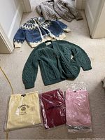 All six sweaters shown together on carpet floor; three cable knits and three new sweaters in packaging