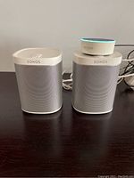 Two white Sonos speakers on dark wood surface with one Amazon Echo Dot on top of right speaker