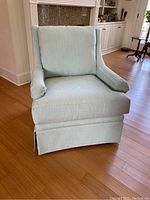 Front view of the light blue upholstered armchair showing the loose back cushion and skirted base.