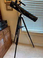 Three-quarter view of black Bushnell telescope mounted on tripod in front of window