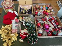 Full view of lot on table showing stockings, garlands, Santa figurines, and boxed candle holders with many glass ornaments in boxes