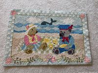Full view of the hooked rug showing the two bears playing in the sand near the ocean with a whale in the background.