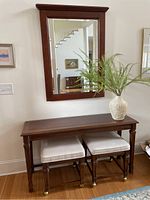 Front view of the console entry set including mirror, console table, two stools with casters, and decorative vase with faux plant on the console.