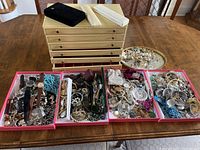 Full view of jewelry chest with six drawers and top storage, four open trays of jewelry laid out on dining table