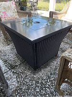 Photo of the entire fire pit table showing woven wicker base and black metal top with removable center lid.