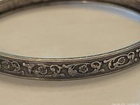 Close-up of silver bangle bracelet with floral scroll engraving pattern