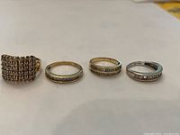 Four gold rings laid side by side: cluster ring, two guard rings, white gold band