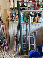 Five fishing rods and green protective case leaning against wall with cleaning supplies behind.