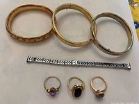 Three gold plated expandable bangles at top, white gold filigree bracelet segment in middle, three gold rings with stones at bottom.