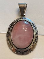 Front view of Native American sterling silver pendant with polished oval rose quartz stone and detailed silver frame.