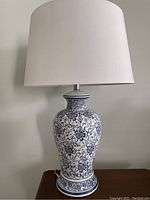 Full view of one blue and white porcelain lamp with white fabric shade on wooden surface