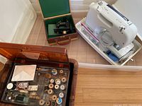 Tray containing white portable machine, small Singer machine case, basket of thread spools