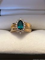 Front view of the ring showing marquise-cut green center stone and surrounding halo of white accent stones