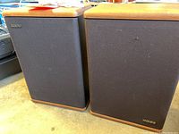 Two Baby Advent speakers side by side showing wood finish tops and bottoms with black fabric grills and 'Advent' logo on the lower right.