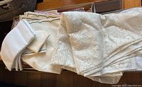 Stack of various folded white table linens including lace tablecloths and embroidered napkins