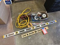 Photo of two carpenter levels, jumper cables and a box of assorted loose hardware items on floor