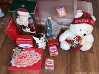 Wide view of assorted Christmas decorations including boxed Santa collectible, white plush bear with red and green hat and scarf, porcelain angel figurine, Christmas greeting cards and wrapping paper.