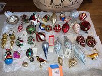Full layout of assorted Christmas ornaments on white tissue, showing various glass, wood, and fabric ornaments with new tags.
