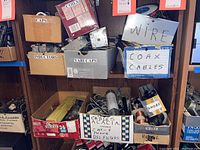 Cardboard boxes labeled Caps, Inductors, Vari Caps, Coax Cables, Wire containing electronic components on shelves