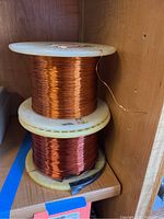 View showing two plastic spools wound with copper wire, one lighter and one darker in color, placed on a wooden shelf.