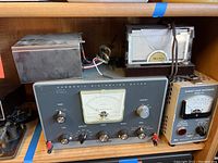 Overall view of three electronic meters: Heathkit Harmonic Distortion Meter, Roto King device, and Waters Dummy Load Watt Meter side by side on a shelf.