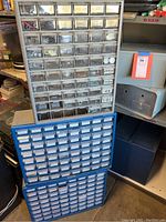 Three multi-drawer cabinets with various small transparent drawers filled with electrical components, nuts, bolts, staples, and hardware items, stacked together.