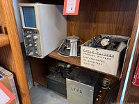 Wide view of shelf showing Tektronix oscilloscope, speaker, and box of electronic parts labeled Little Kludges.