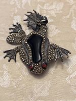 Front view showing the detailed jeweled frog brooch with black central stone and red eyes.