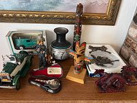Overall view of the collectibles displayed on a wooden surface including diecast car, miniature guitars in cases, tiki totem, vase, plate and figurines.