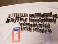 Wide shot of approximately 60 small vacuum tubes laid out on a cloth surface, showing multiple types and sizes