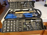 Open black plastic carrying case showing organized tools including sockets, wrenches, pliers, screwdrivers, and hammer