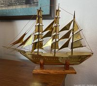 Side view of vintage brass and tin ship model on wooden base showing three masts with brass sails and copper wire rigging.