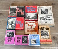 Photo of all nine puzzle boxes laid out on a wooden floor, showing brand names, titles, and some artwork on boxes.