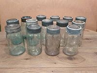 Front view of 14 Mason jars arranged in two rows showing various clear and green glass jars with zinc ring lids.
