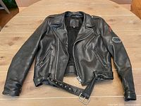 Front view of the black leather motorcycle jacket with belt and zippered pockets.