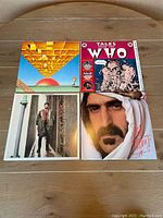 Four vinyl album covers on a wooden surface showing Monty Python, The Who's "Tales from The Who," The Who's "Quadrophenia" and Frank Zappa's "Sheik Yerbouti."