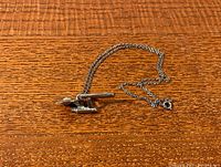 Photo of the Star Trek Enterprise pendant and chain laid out on wood surface, showing side profile view of pendant.