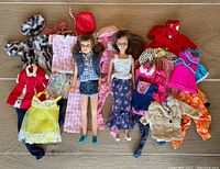 Photo showing two vintage Barbie sister dolls surrounded by a collection of assorted vintage doll clothes including coats, dresses, and hats.
