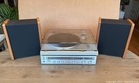 Front view of turntable with dust cover closed flanked by two wood-edged speakers on table
