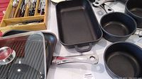 Cookware set showing saucepans, Dutch oven, frying pans, stove top grill, three section flat pan, and silverware set in wooden box.
