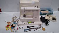 Kenmore sewing machine with foot pedal, measuring tape, scissors, needles, bobbins, spare parts, and carrying case displayed together on a flat surface