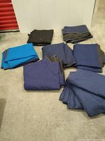Six moving blankets laid out and folded on a floor, showing colors and texture.