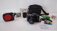 Photo showing Canon EOS 10s SLR camera with attached 50mm lens, Canon 35-105mm zoom lens, Canon PowerShot S1 IS digital camera, camera case, batteries, film pack, and accessories on white table.